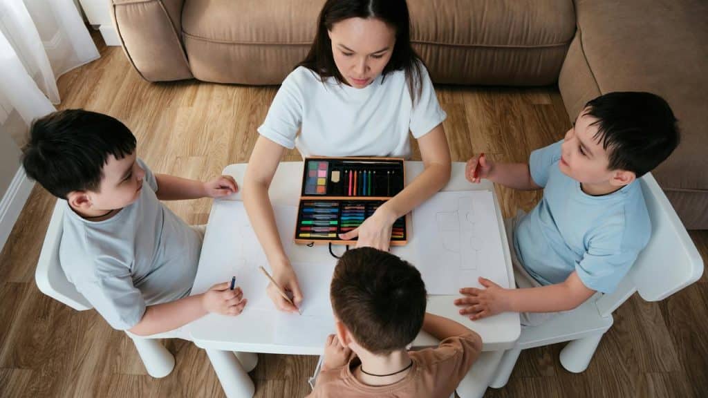 A teacher helping kids draw with colored pencils at a small table.