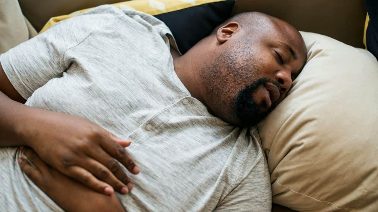 A man is sleeping on a couch with his hand resting on his stomach.