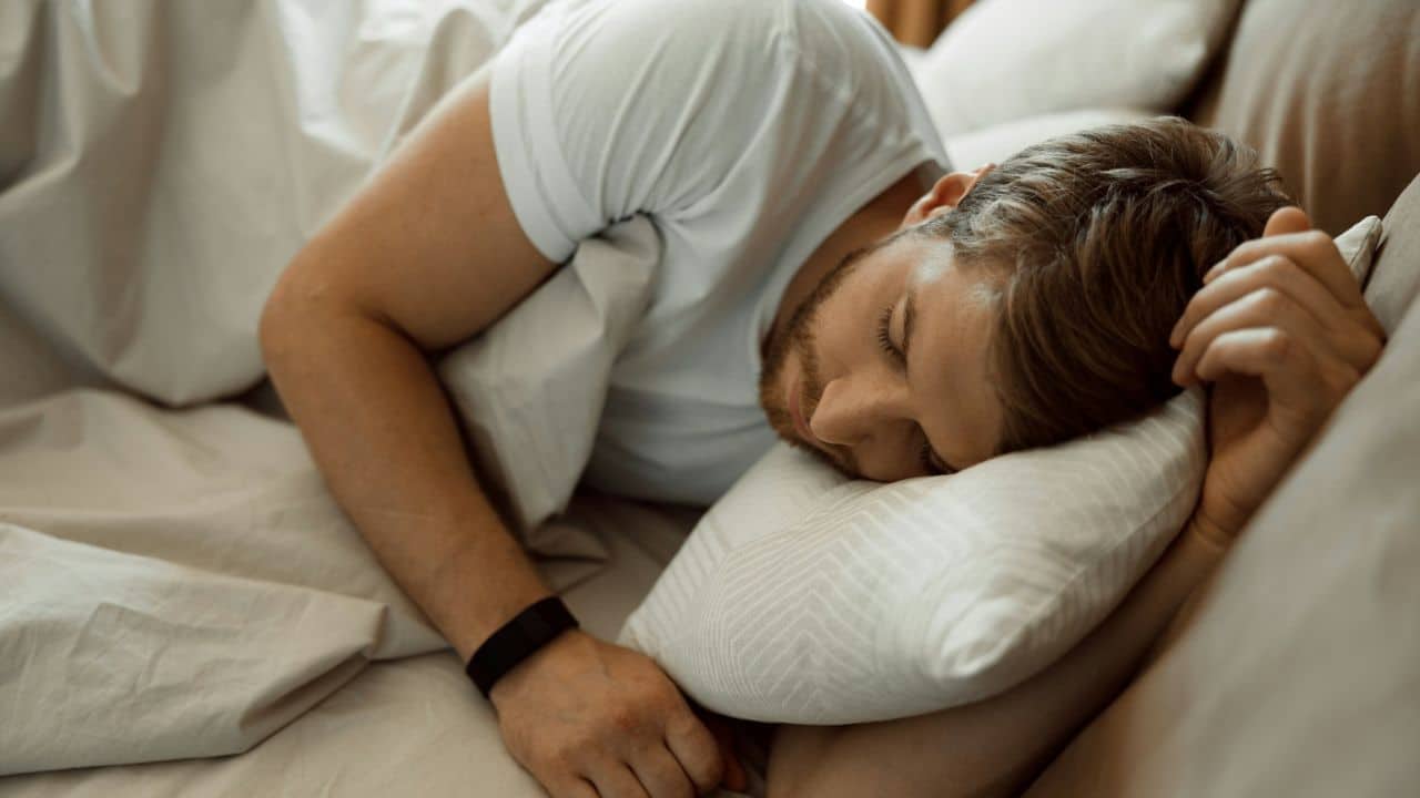 A man with a beard is sleeping on his side in a bed.