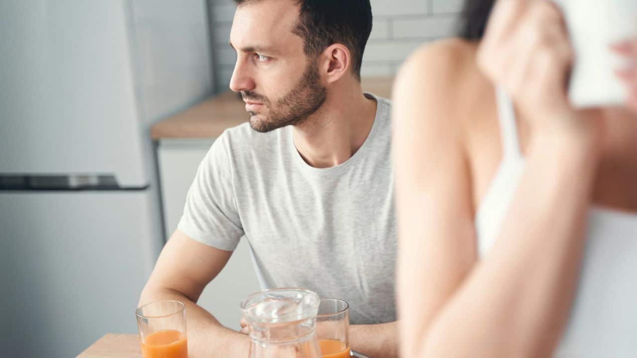 A man sits at a table with juice and looks away from a woman sitting across from him.