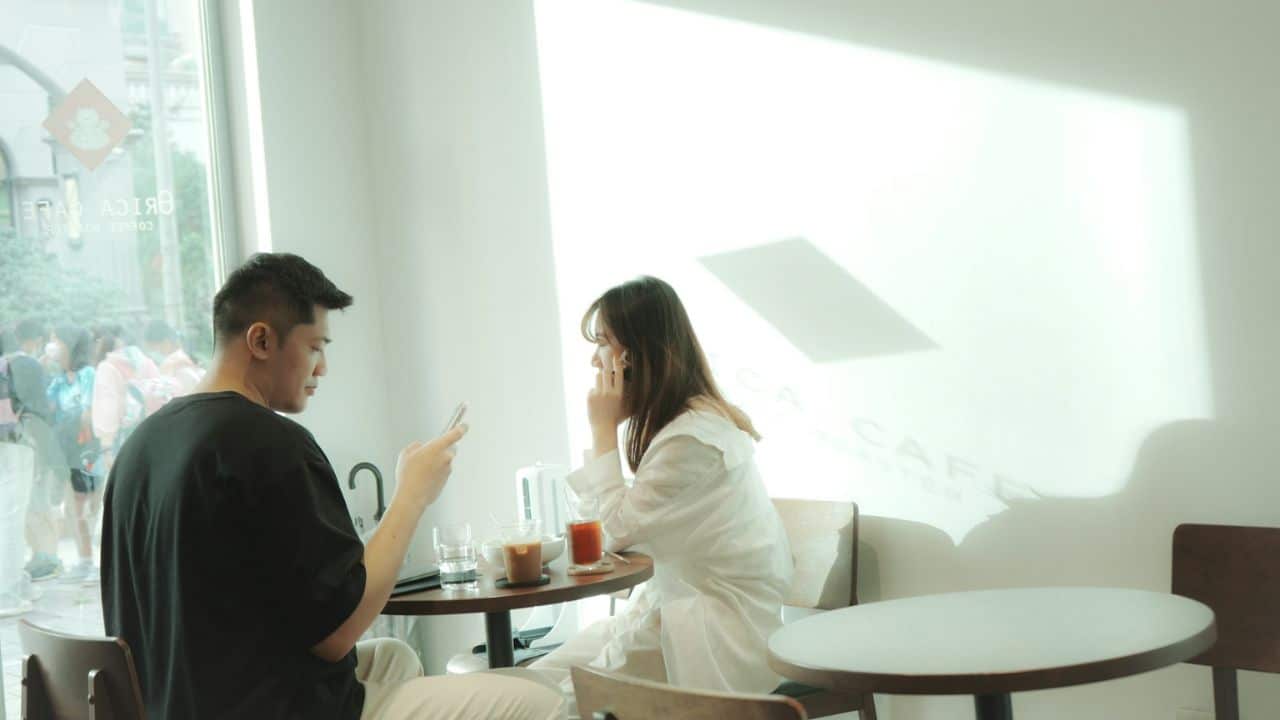 A man and a woman sit at a cafe table, with the man looking at his phone.