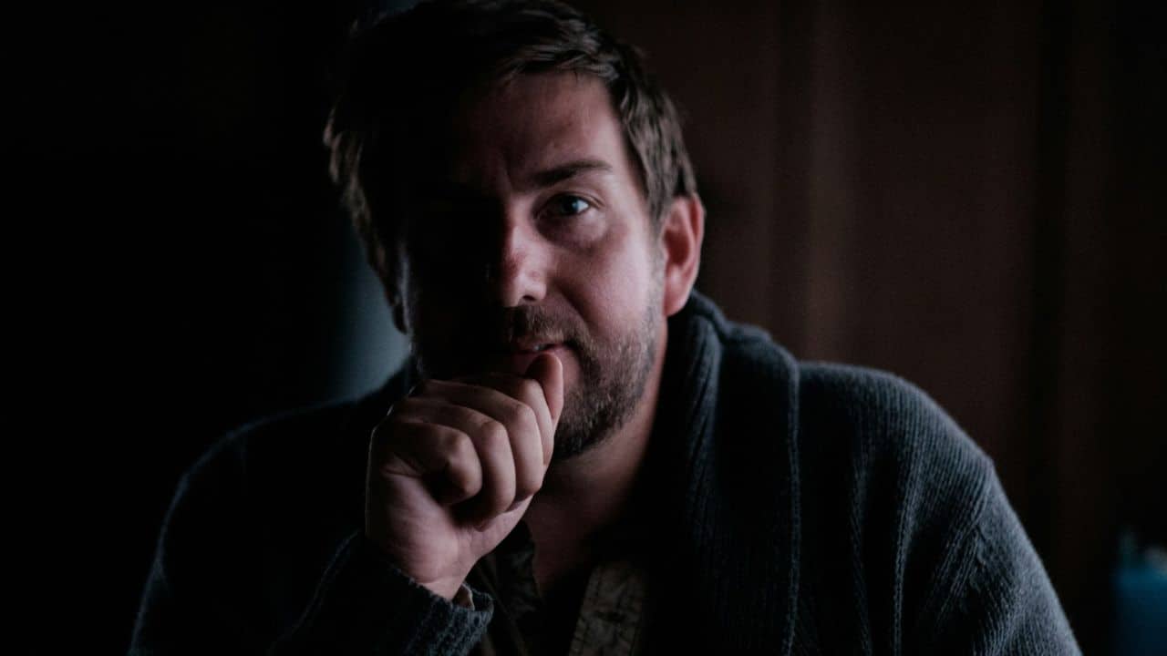 A man with his hand on his chin looks at the camera.