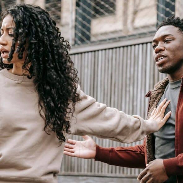 A woman with curly hair pushes a man's hand away as he tries to touch her arm.