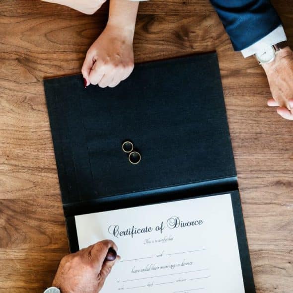 A high-angle view of two people signing a divorce certificate, with wedding rings on top.