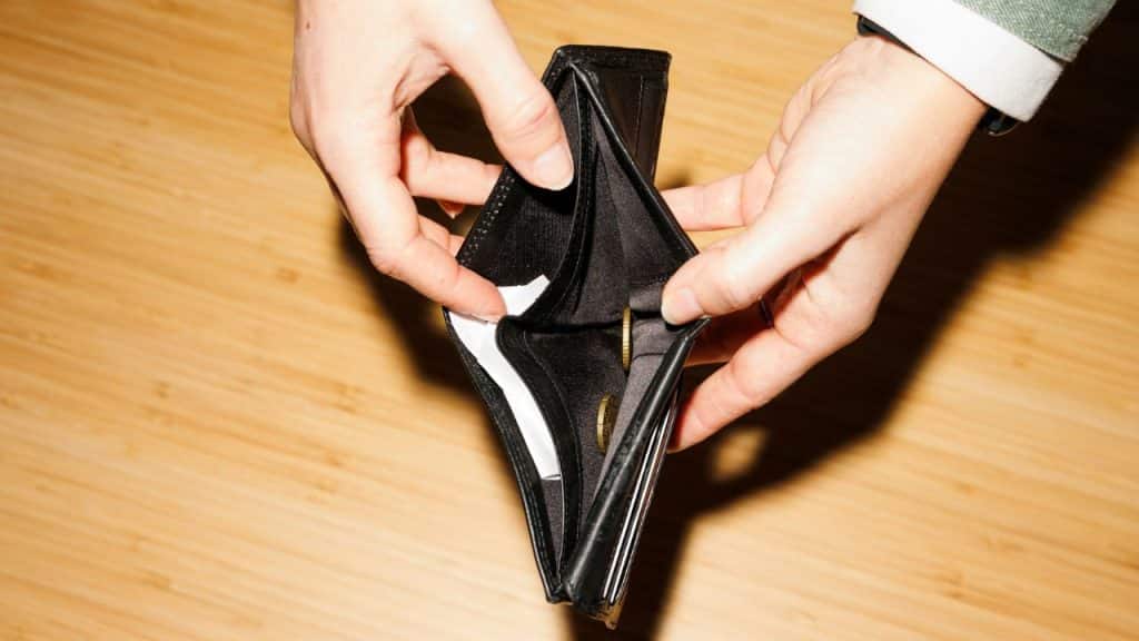A pair of hands holds an empty wallet with only a few coins inside.