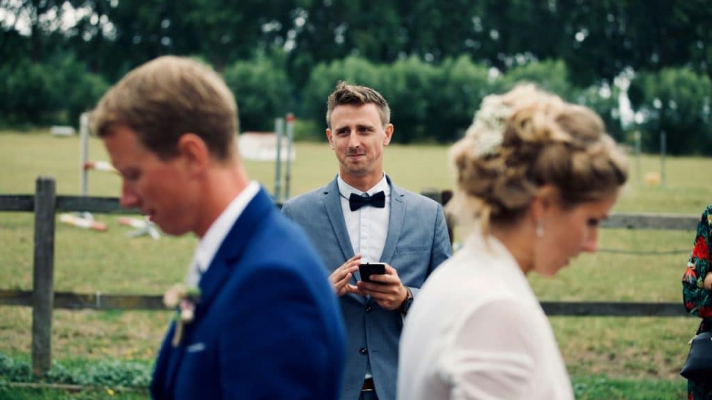A groom in a bow tie smiles mischievously while looking at his phone.