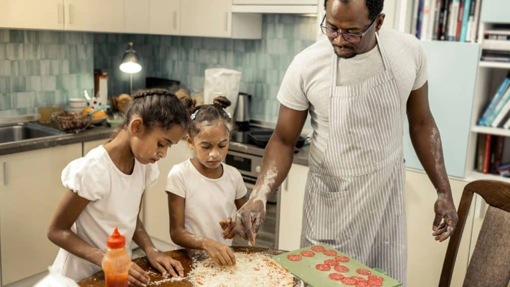 A father and his two daughters are making a pizza together in the kitchen.