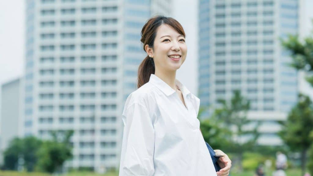A young, happy woman in a white shirt stands outside with buildings in the background.