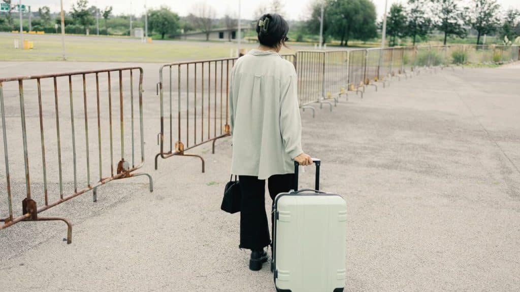 A woman walks away with a suitcase, leaving an empty, fenced area behind.