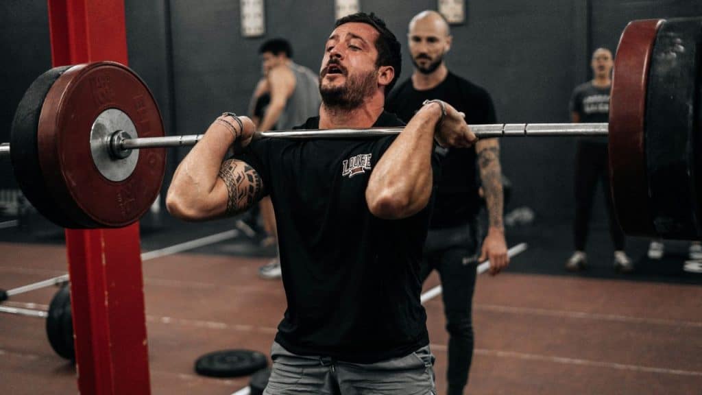 A determined man lifts a heavy barbell, straining with effort in a gym.