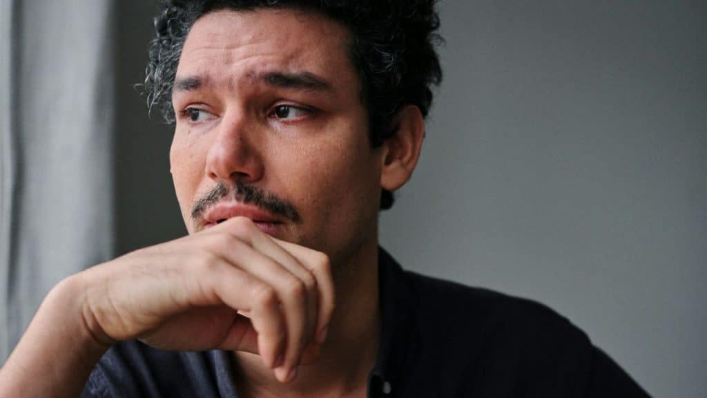 A man with a pensive expression is holding his hand to his chin.