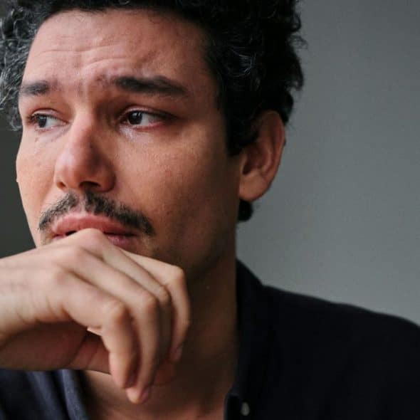 A man with a pensive expression is holding his hand to his chin.
