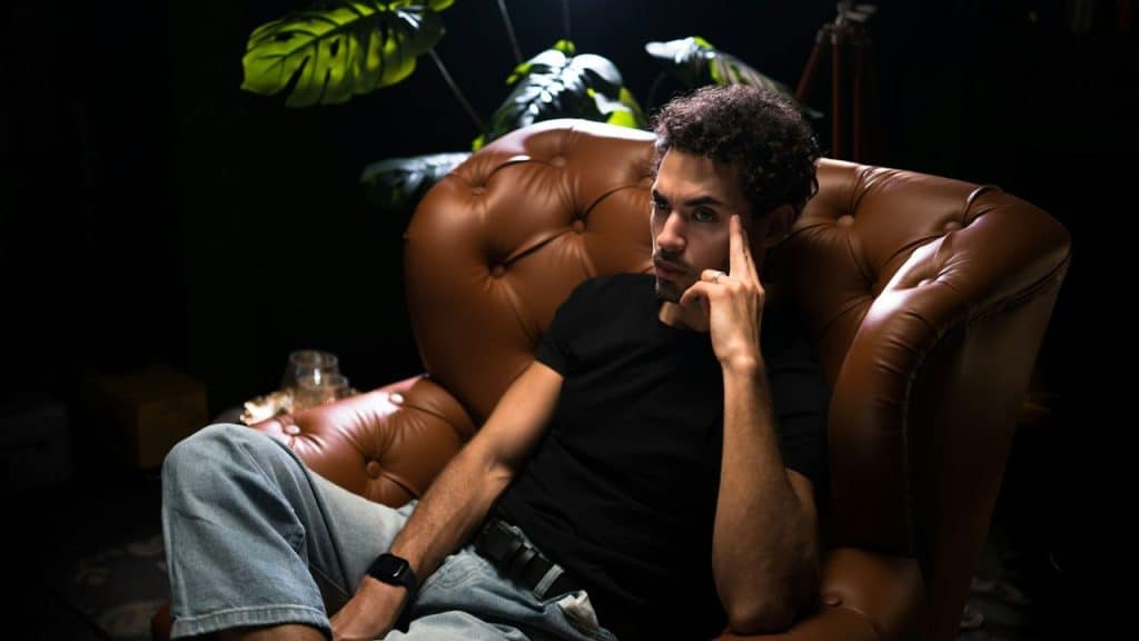 A man sits pensively in a brown leather armchair.