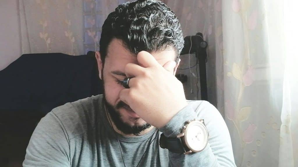A frustrated man is sitting with his hand covering his face.