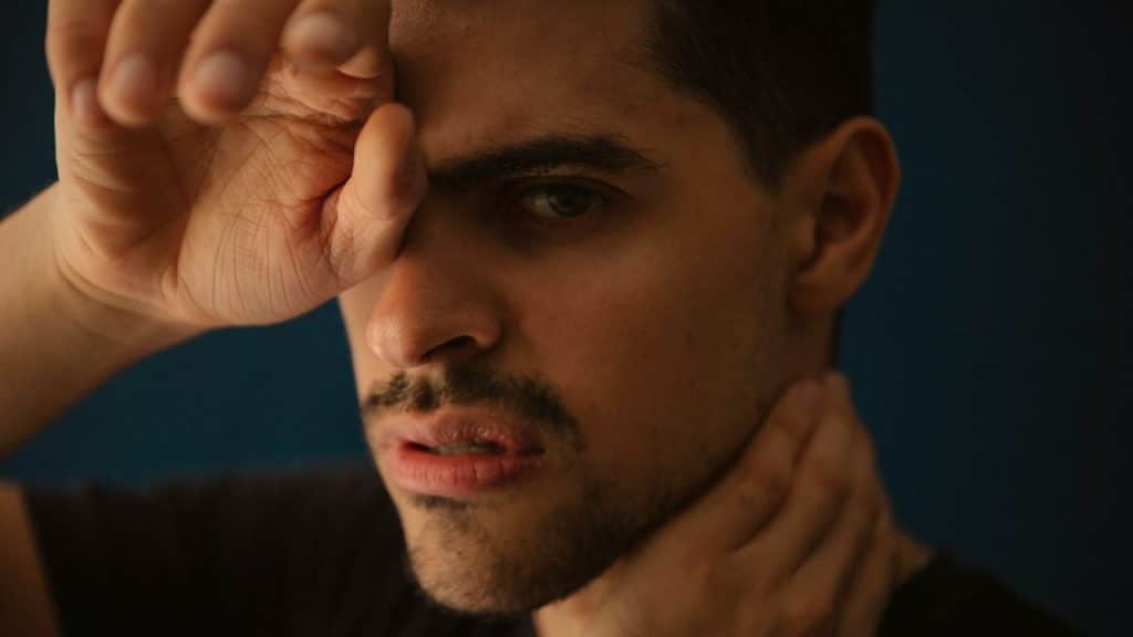 A worried man is looking at the camera with his hand covering his face.
