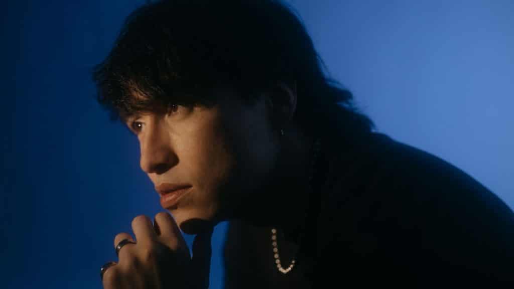 A thoughtful man in a dark shirt and rings looks to the side.
