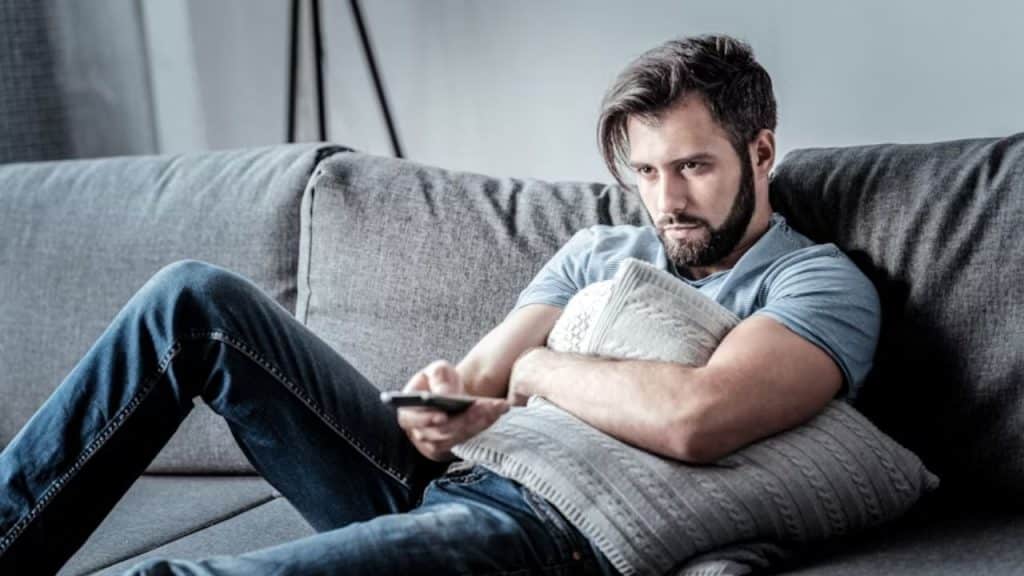 Man feeling unhappy, slouching and watching TV while neglecting fitness