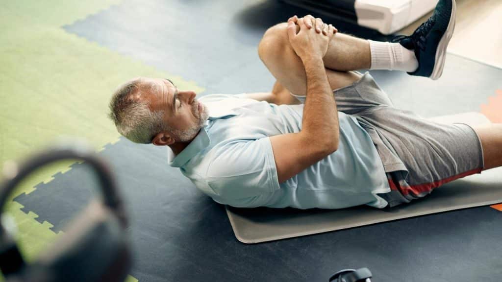 A middle-aged man stretching on a gym mat.
