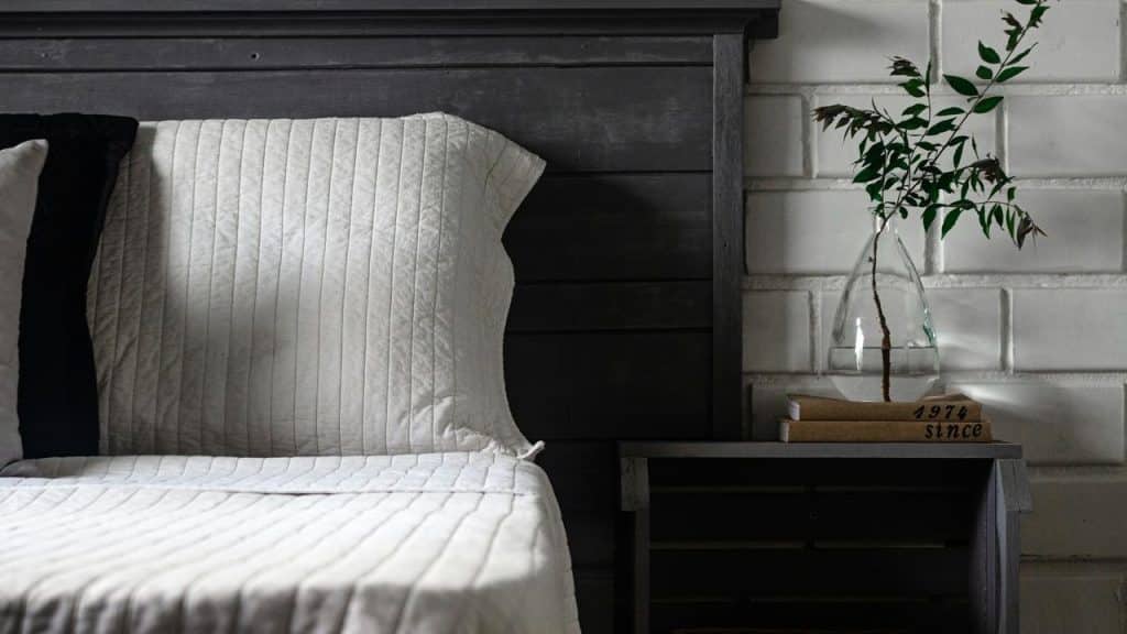 A bed with white bedding and a nightstand with a vase.
