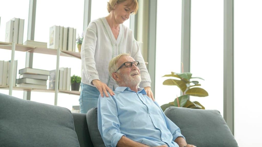 A woman gives a man a shoulder massage on a couch.