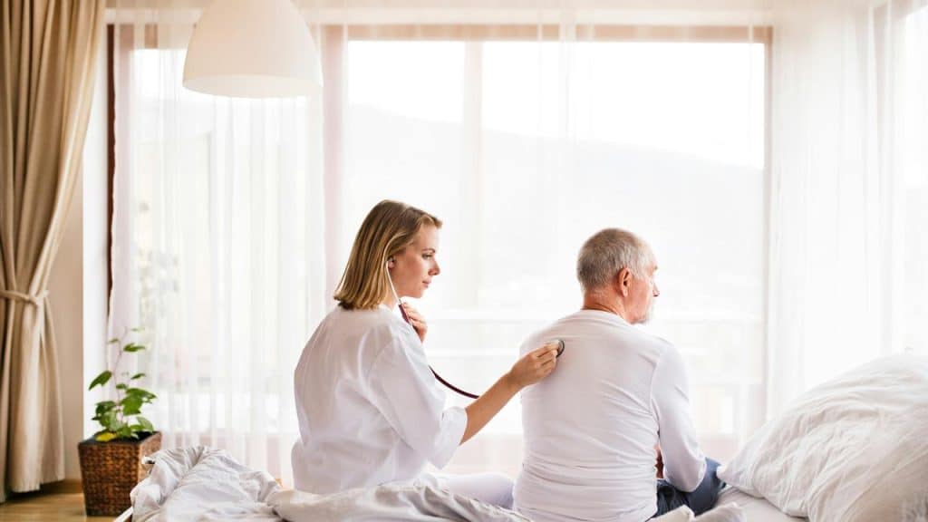 A nurse checks an elderly man's back with a stethoscope.