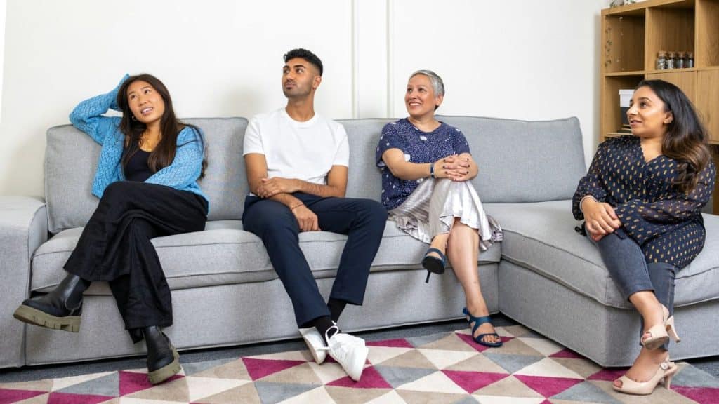 A multi-ethnic family of four sits on a gray couch, looking up and right.