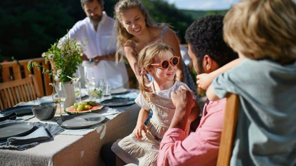 A group of adults and kids enjoying an outdoor meal together on a sunny day.