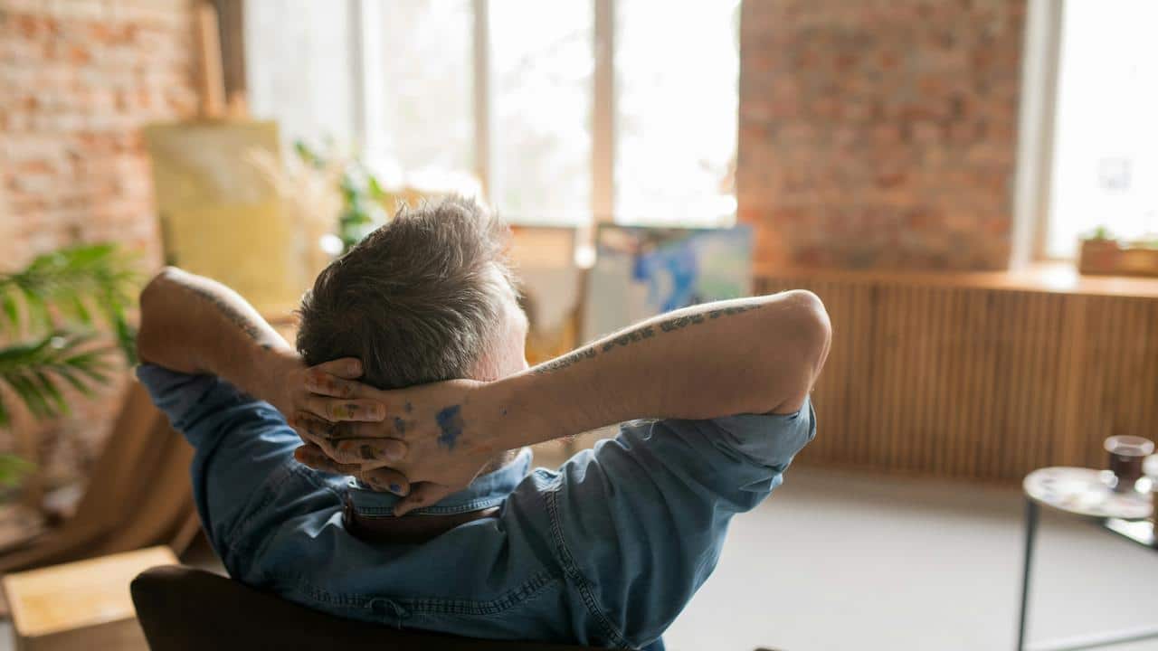 A man with paint-stained hands relaxes in an art studio.