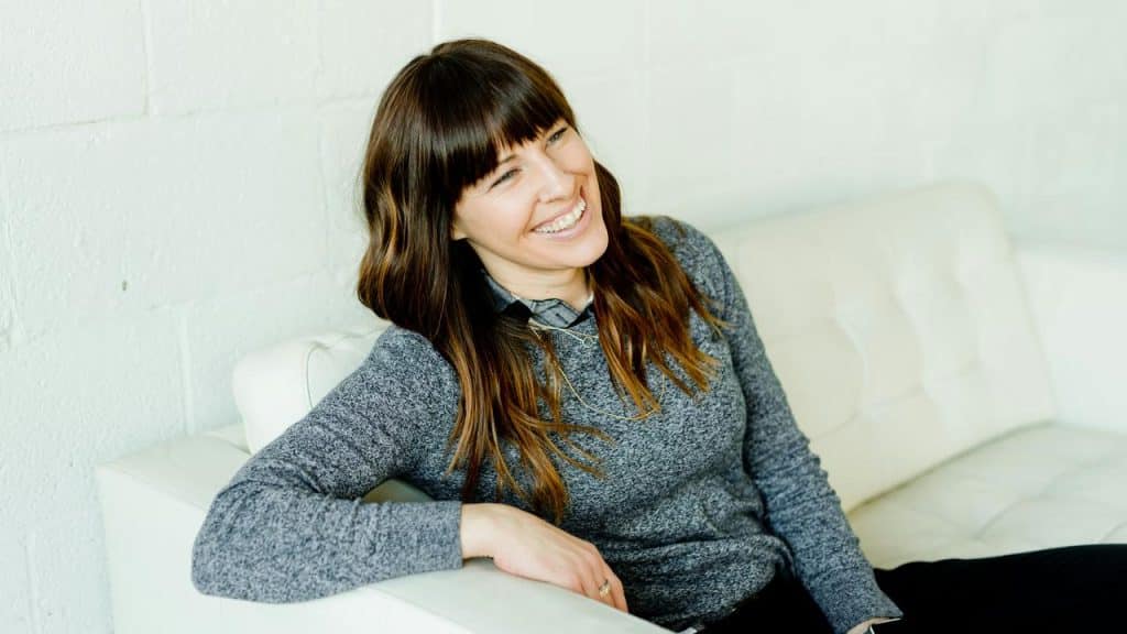 A woman smiling while sitting on a white couch.