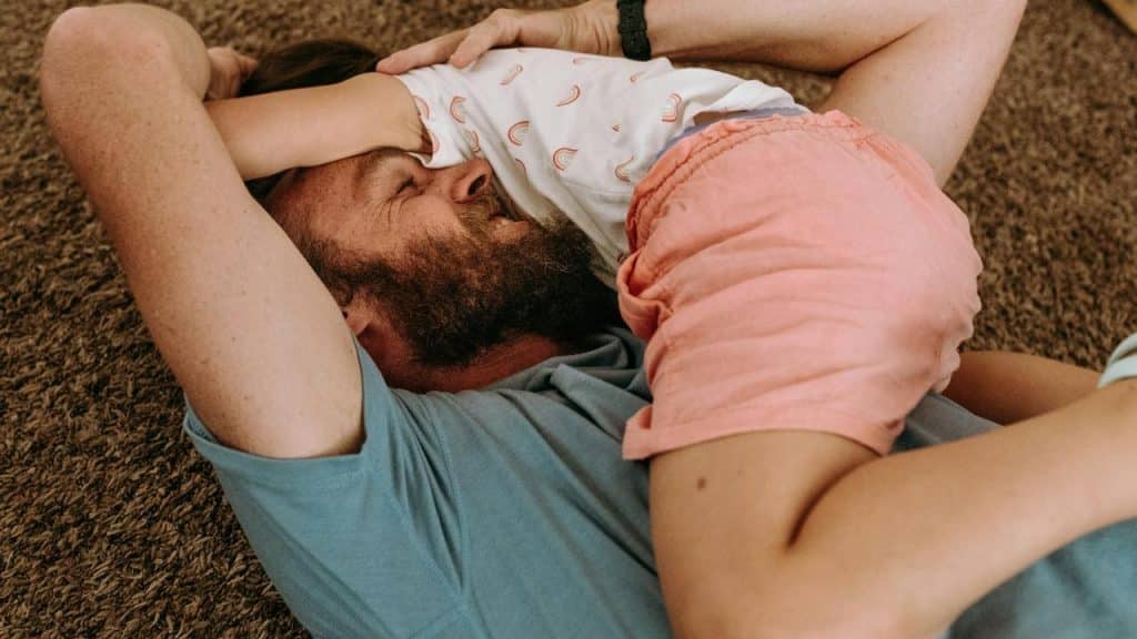 A man lying on the floor playing with a child.