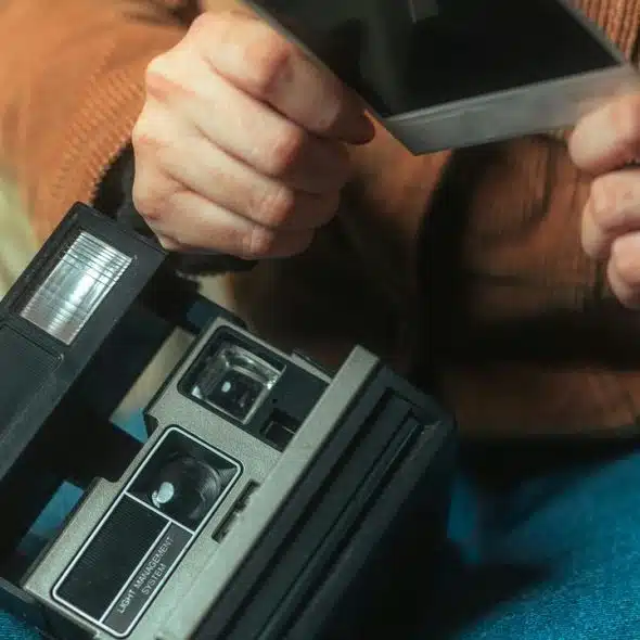 A person holding a Polaroid photo and instant camera.