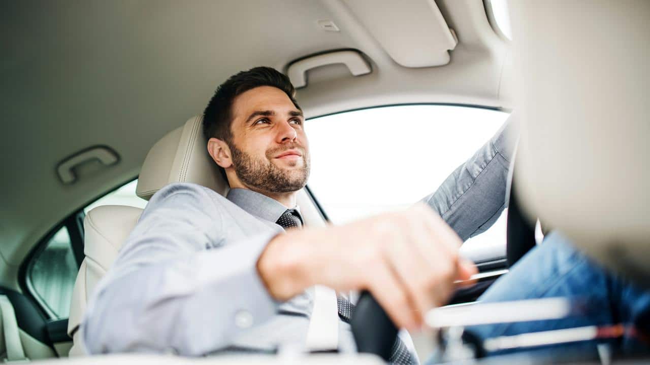 A man in a shirt and tie drives a car..