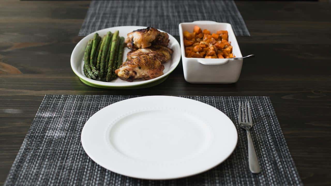 A plate of roasted chicken, asparagus, and sweet potatoes on a table.