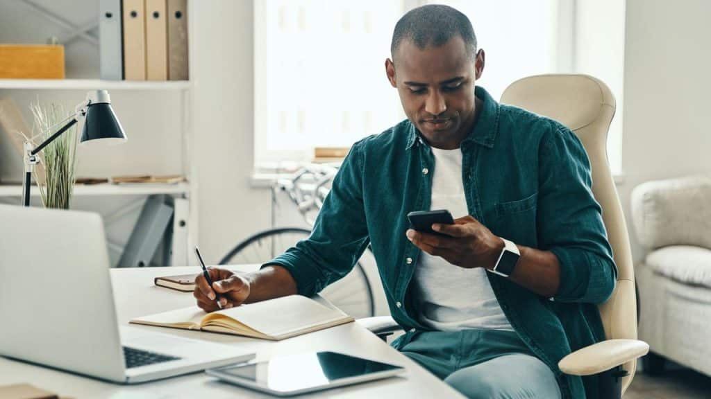 A man working at a desk while looking at his phone.