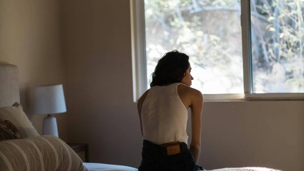 A person sitting on a bed and looking out the window.