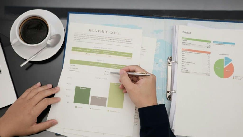 A person reviews financial documents and charts, with a cup of coffee nearby.