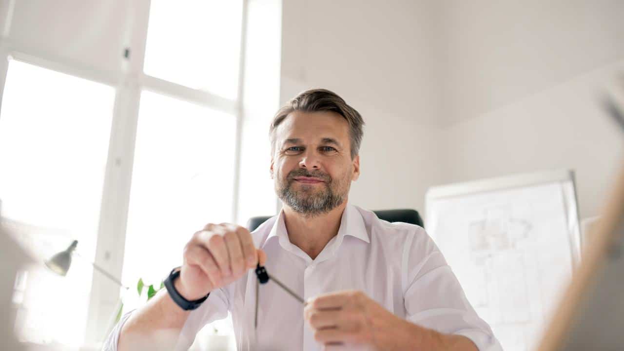 A man in a white shirt holds a compass at a desk.