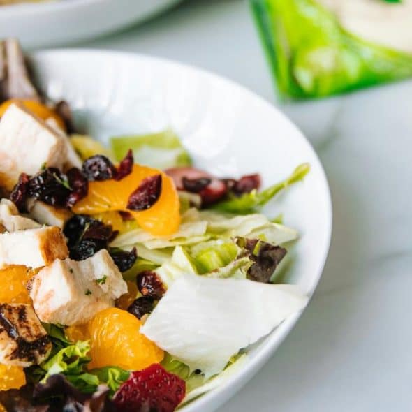 A bowl of salad with grilled chicken, mandarin oranges, dried cranberries, and mixed greens.