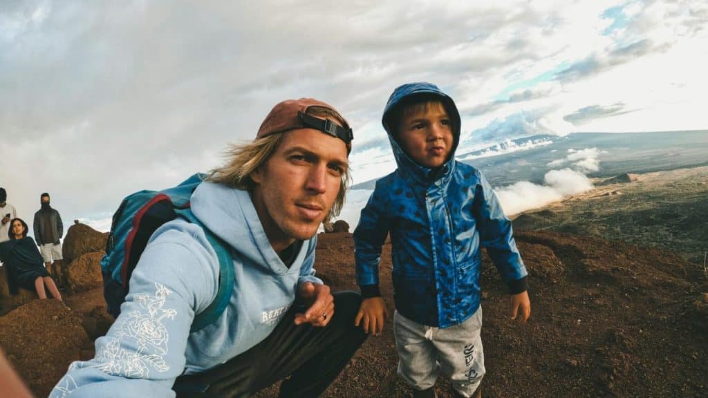 A man and a kid posing on a mountain trail with a scenic view.