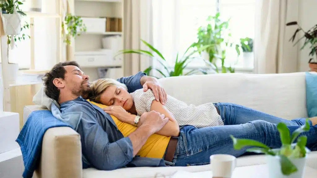 A couple napping together on a white couch at home.