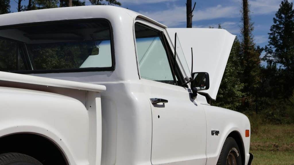 A white vintage pickup truck with the hood open.