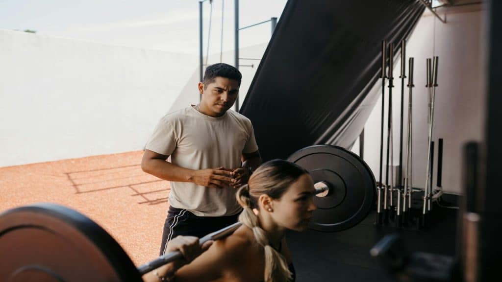 A man watching his girl lifting weights.