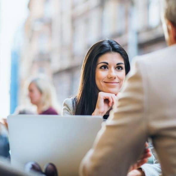 A woman smiling while talking to a man at an outdoor café.