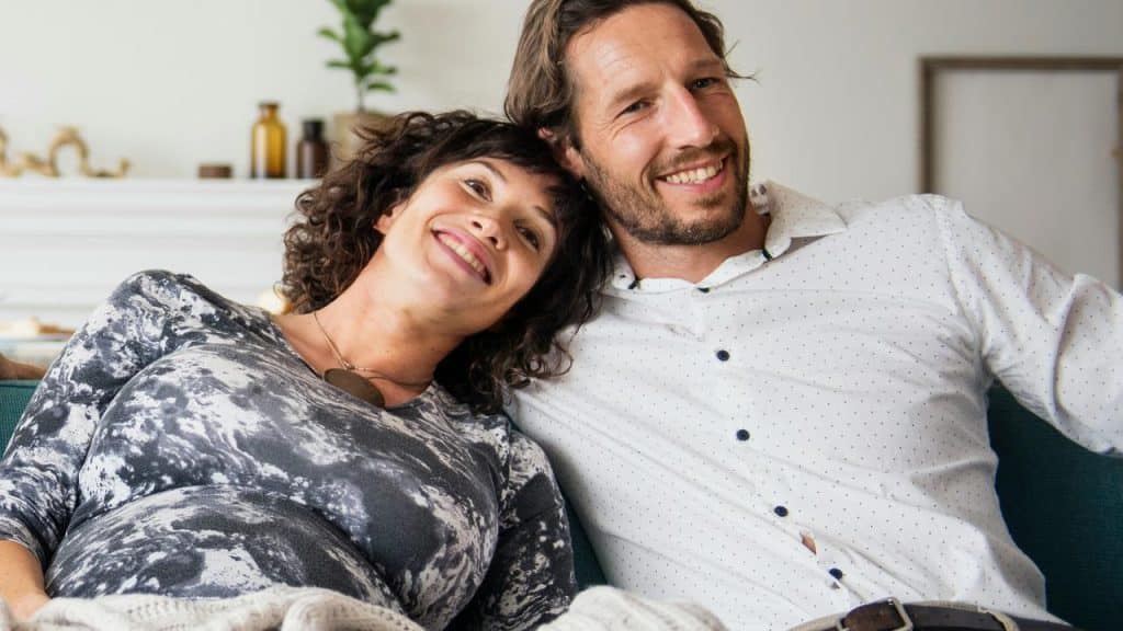 A couple smiling while sitting close together on a couch.
