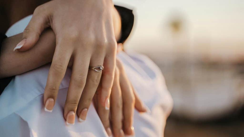 An engagement ring on a hand resting on someone's shoulder.