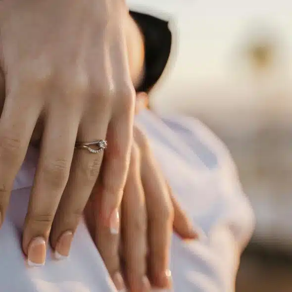 An engagement ring on a hand resting on someone's shoulder.