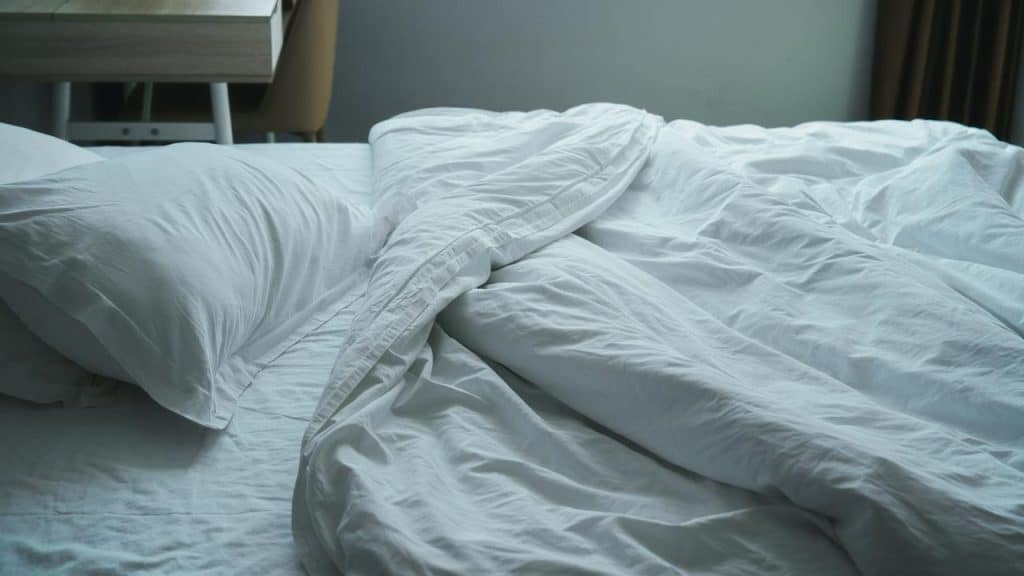A messy bed with white sheets and pillows in soft light.