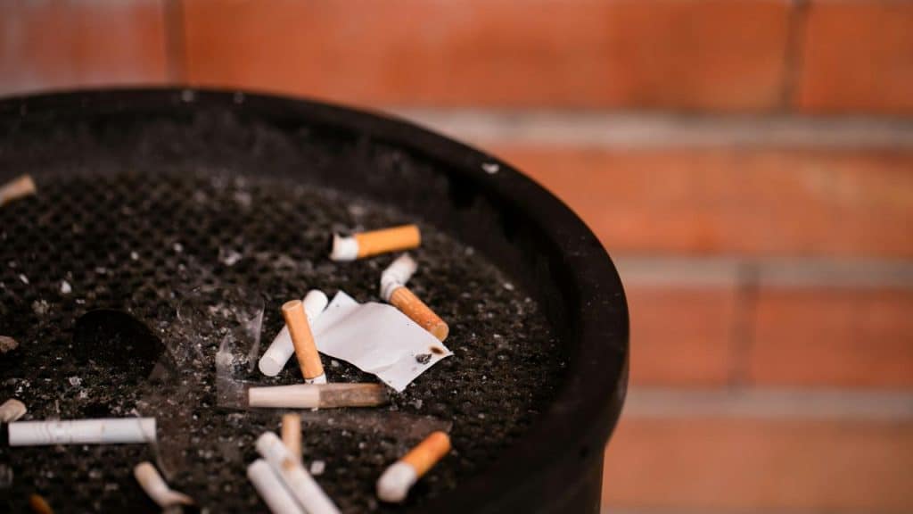 A dirty ashtray filled with cigarette butts and trash.