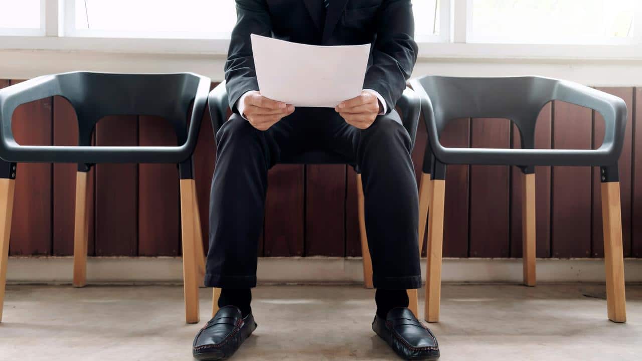 A man in a suit holding papers while seated in a waiting area.