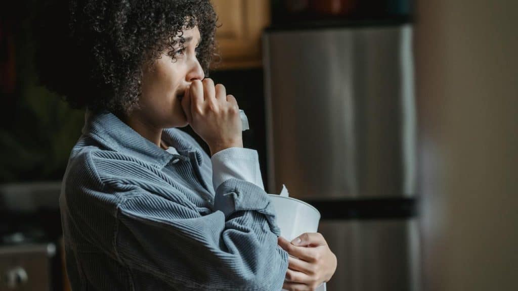 A woman holding a tissue and looking thoughtful in a kitchen.